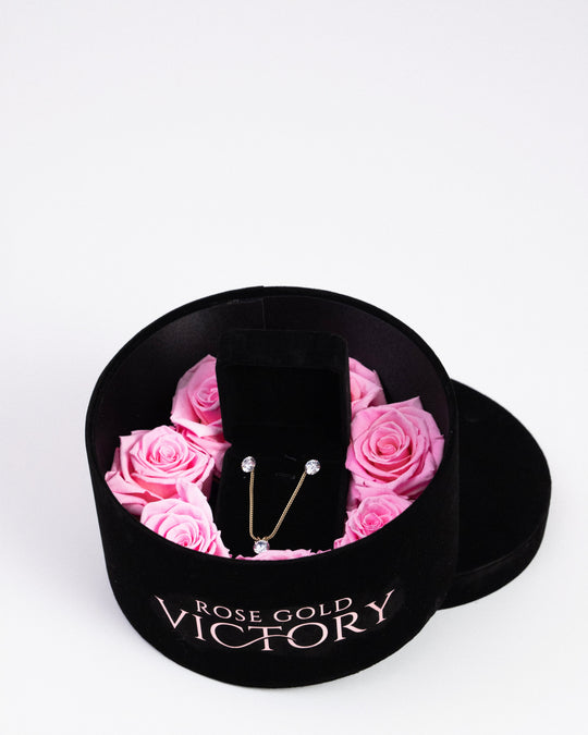 Pink preserved roses with a gold jewelry set in a black round box — Rose Gold Victory