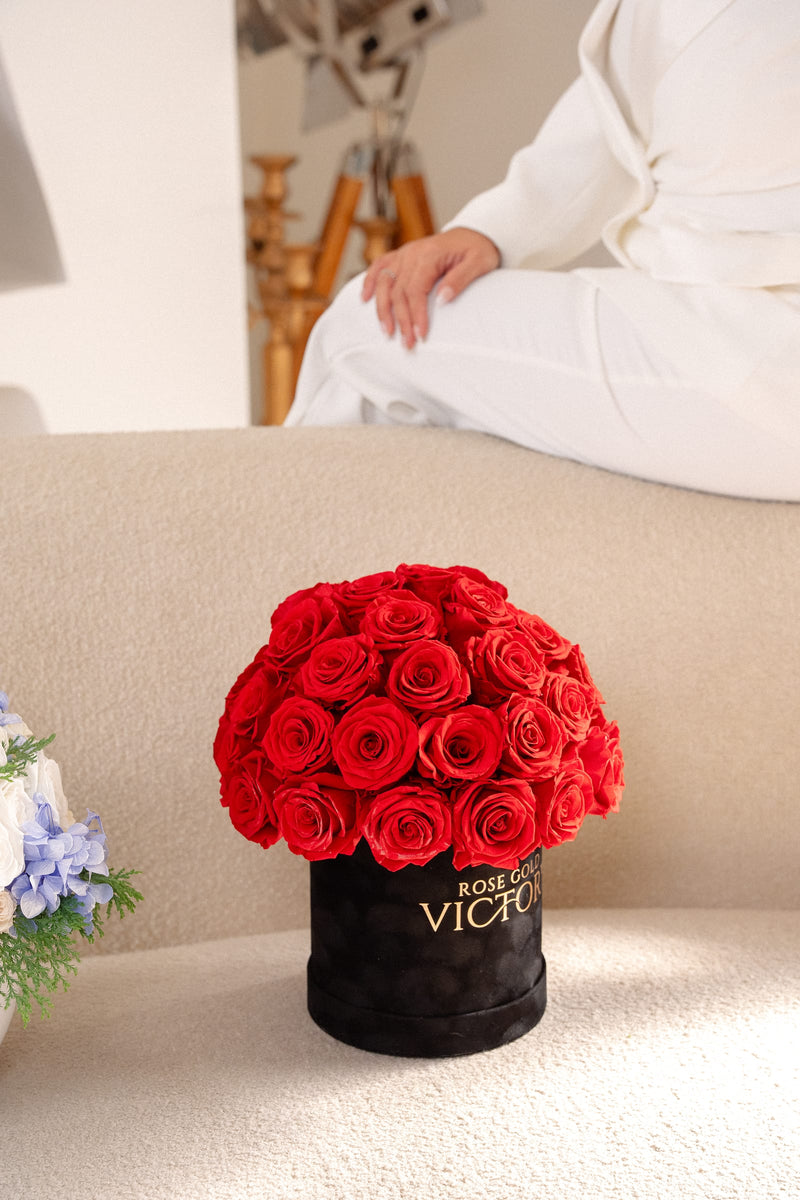 Rose Gold Victory red preserved-rose dome box styled on a curved cream sofa